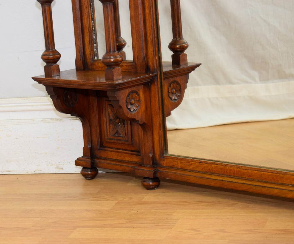 A Victorian carved oak overmantel mirror featuring turned side columns, small side display shelves, an arched pediment, and mirrored glass panels. View XVI