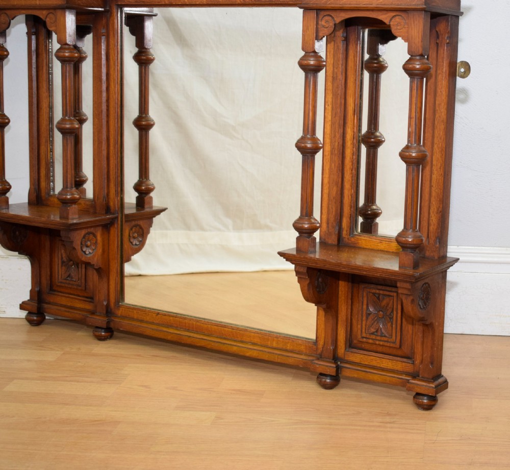 A Victorian carved oak overmantel mirror featuring turned side columns, small side display shelves, an arched pediment, and mirrored glass panels. View XVIII