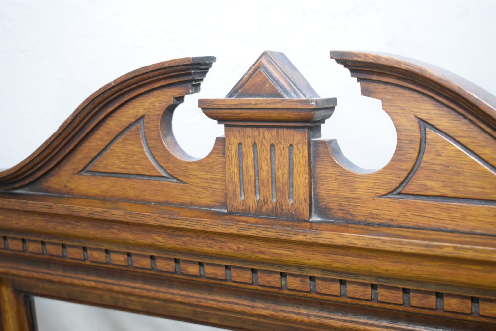 A Victorian carved oak overmantel mirror featuring turned side columns, small side display shelves, an arched pediment, and mirrored glass panels. View XXI