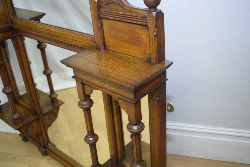 A Victorian carved oak overmantel mirror featuring turned side columns, small side display shelves, an arched pediment, and mirrored glass panels. View XXIII