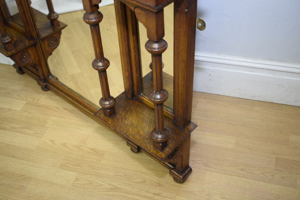 A Victorian carved oak overmantel mirror featuring turned side columns, small side display shelves, an arched pediment, and mirrored glass panels. View XXIV