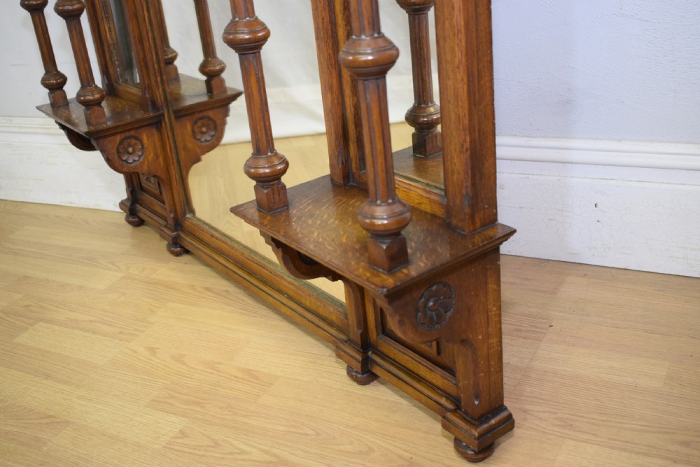 A Victorian carved oak overmantel mirror featuring turned side columns, small side display shelves, an arched pediment, and mirrored glass panels. View XXVII