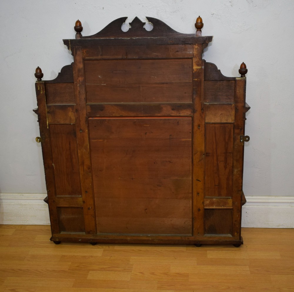 A Victorian carved oak overmantel mirror featuring turned side columns, small side display shelves, an arched pediment, and mirrored glass panels. View XXIX