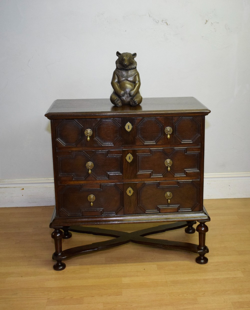 A dark oak Jacobean style cabinet on stand featuring geometric moulded drawer fronts, brass drop handles, turned legs, and an X-shaped stretcher. View II