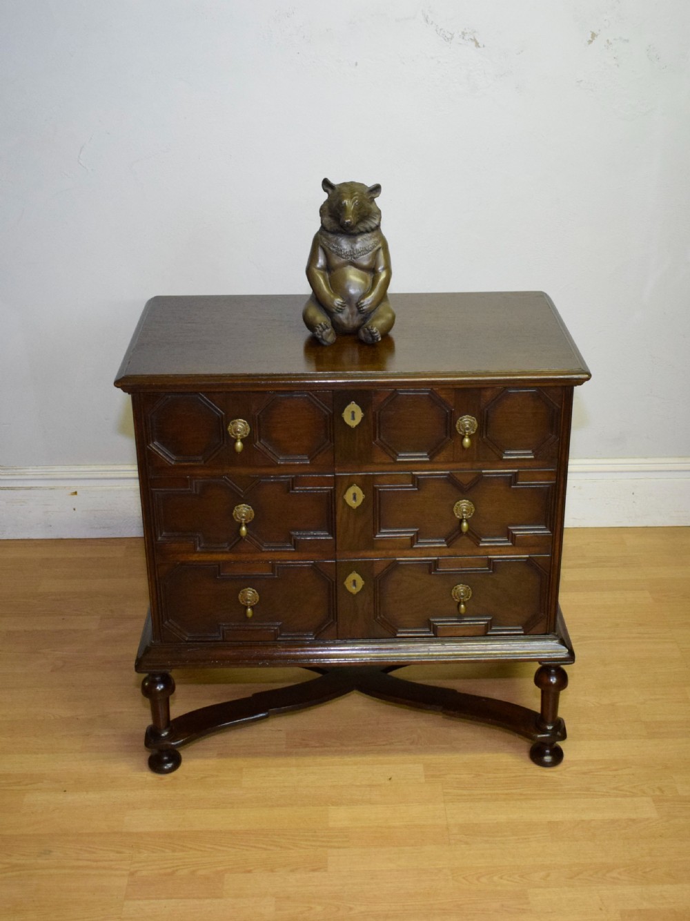 A dark oak Jacobean style cabinet on stand featuring geometric moulded drawer fronts, brass drop handles, turned legs, and an X-shaped stretcher. View VIII