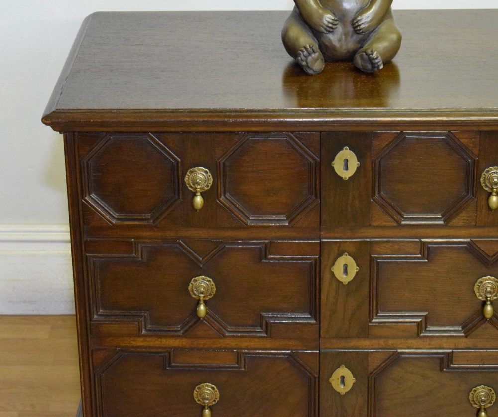 A dark oak Jacobean style cabinet on stand featuring geometric moulded drawer fronts, brass drop handles, turned legs, and an X-shaped stretcher. View IX