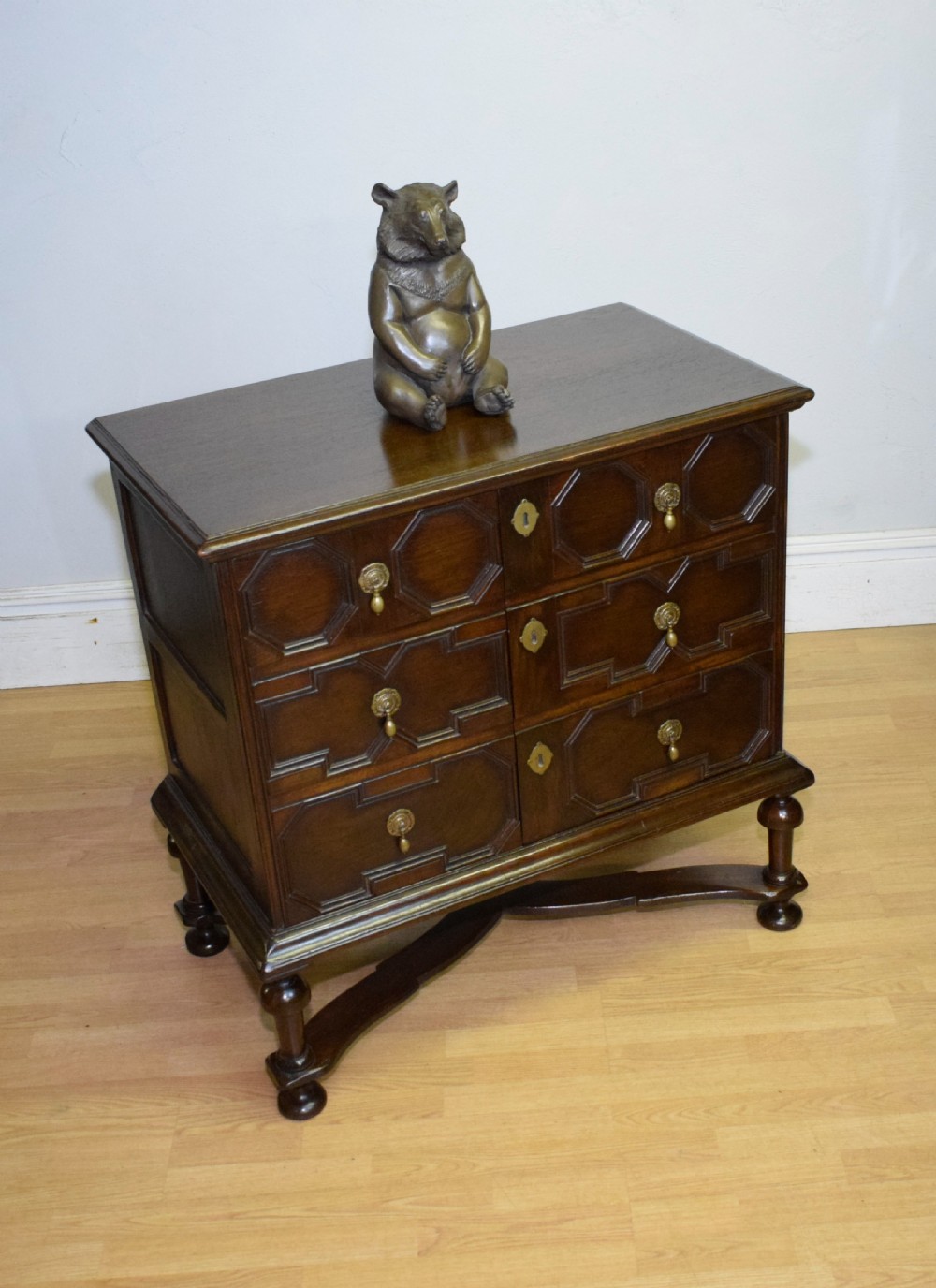 A dark oak Jacobean style cabinet on stand featuring geometric moulded drawer fronts, brass drop handles, turned legs, and an X-shaped stretcher. View XI