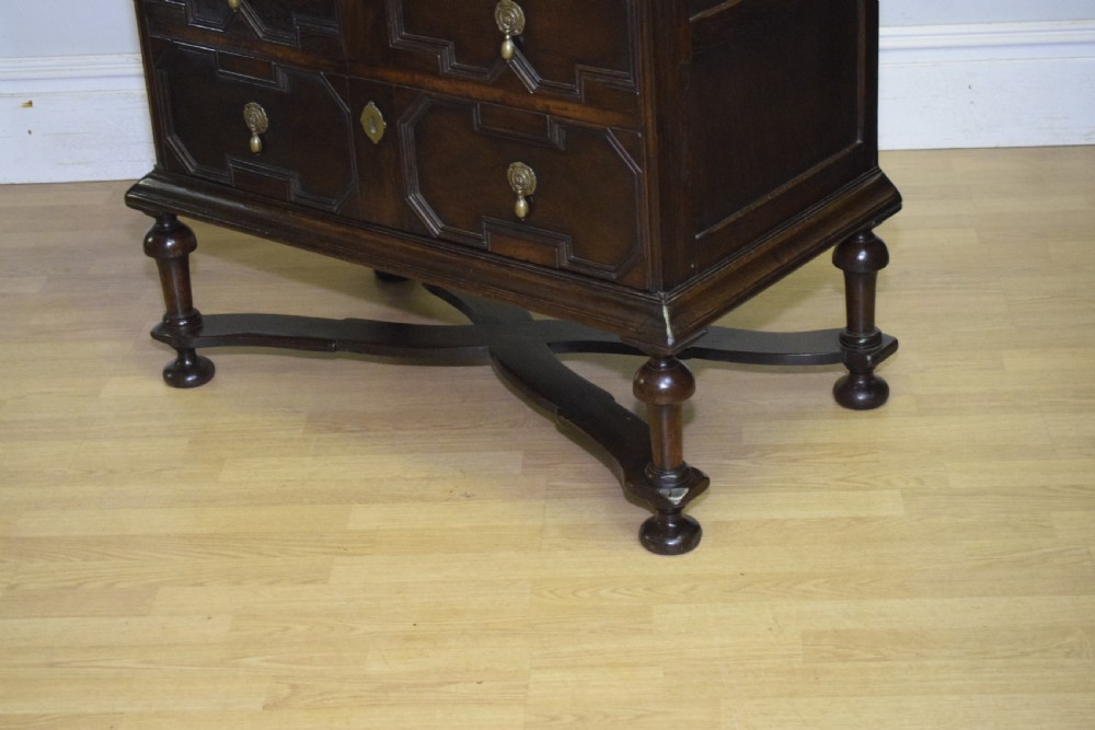 A dark oak Jacobean style cabinet on stand featuring geometric moulded drawer fronts, brass drop handles, turned legs, and an X-shaped stretcher. View XIV