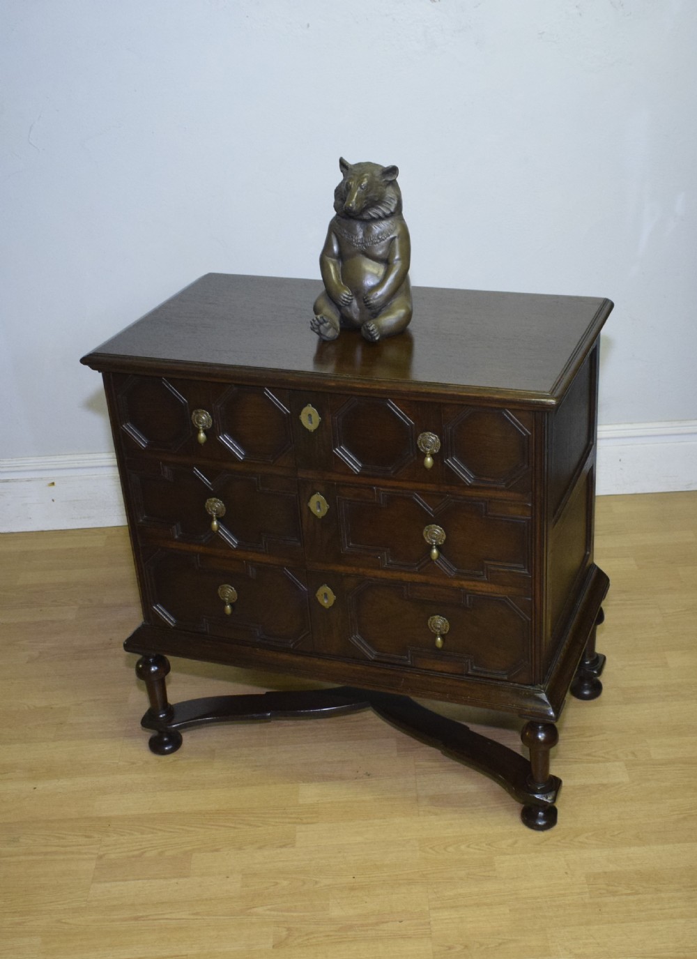 A dark oak Jacobean style cabinet on stand featuring geometric moulded drawer fronts, brass drop handles, turned legs, and an X-shaped stretcher. View XVI