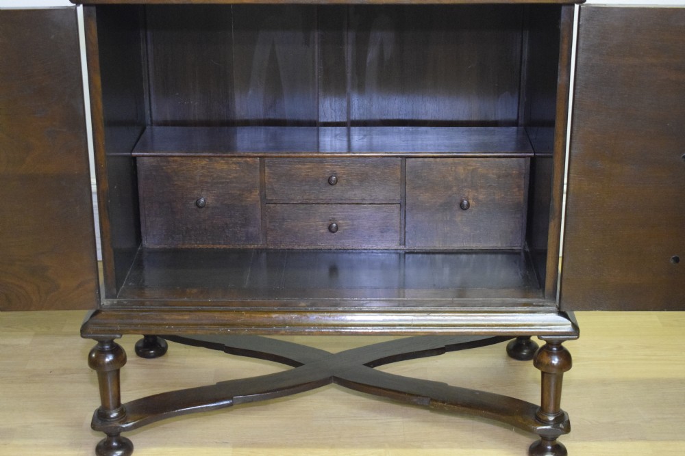 A dark oak Jacobean style cabinet on stand featuring geometric moulded drawer fronts, brass drop handles, turned legs, and an X-shaped stretcher. View XIX