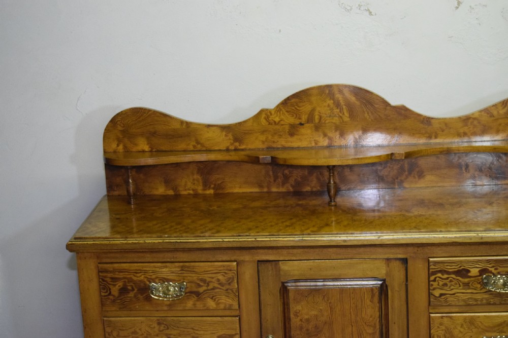 A Victorian golden pine dresser base featuring six drawers, a central panelled cupboard door, brass handles, and a shaped gallery back with a small shelf. View VII