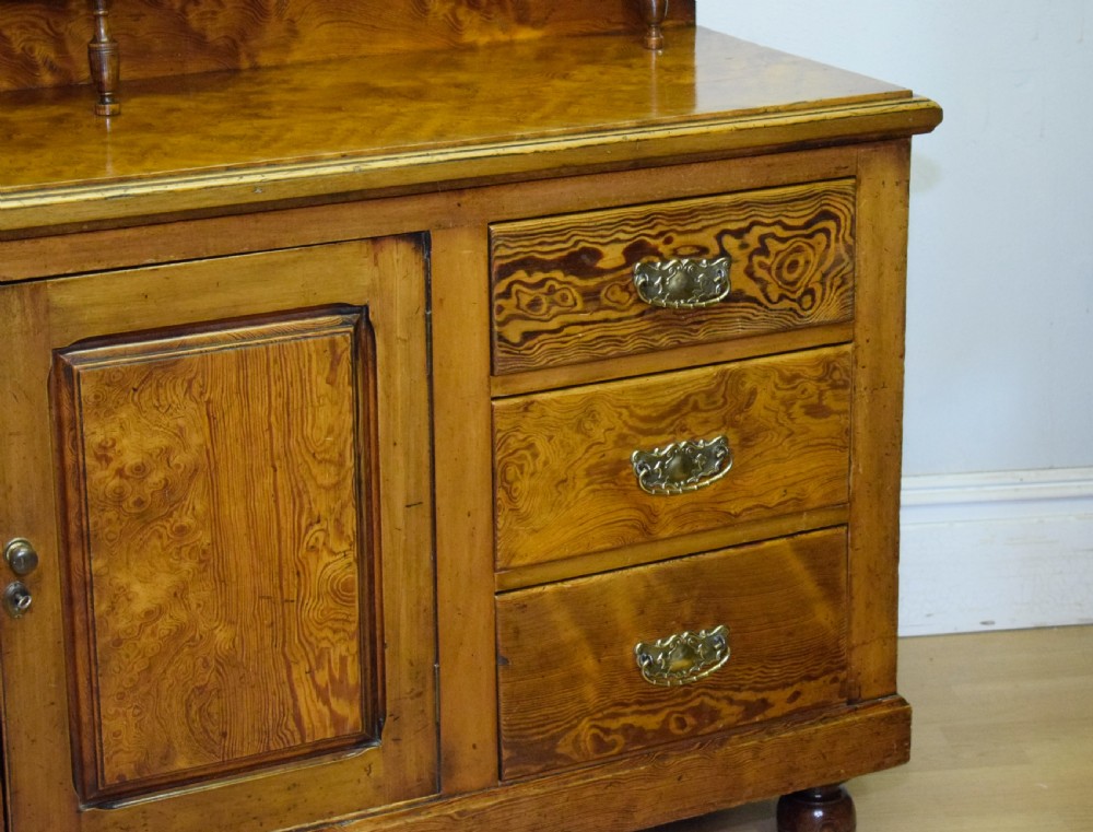 A Victorian golden pine dresser base featuring six drawers, a central panelled cupboard door, brass handles, and a shaped gallery back with a small shelf. View IX