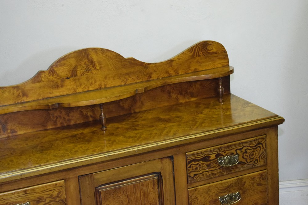 A Victorian golden pine dresser base featuring six drawers, a central panelled cupboard door, brass handles, and a shaped gallery back with a small shelf. View XI