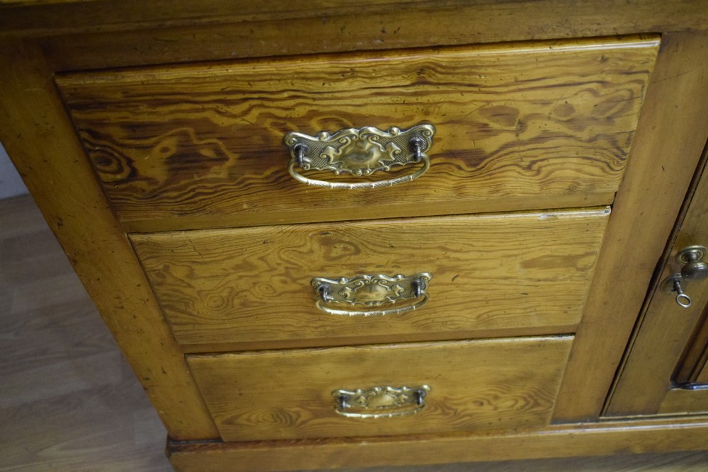 A Victorian golden pine dresser base featuring six drawers, a central panelled cupboard door, brass handles, and a shaped gallery back with a small shelf. View XIX