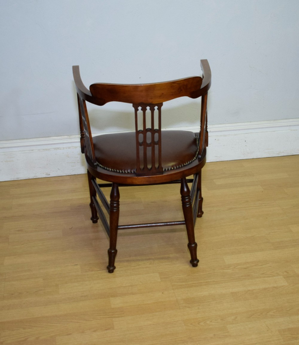A Victorian dark mahogany tub armchair featuring a curved backrest with pierced vertical splats and a brown leather padded seat secured with brass studs. View XVI