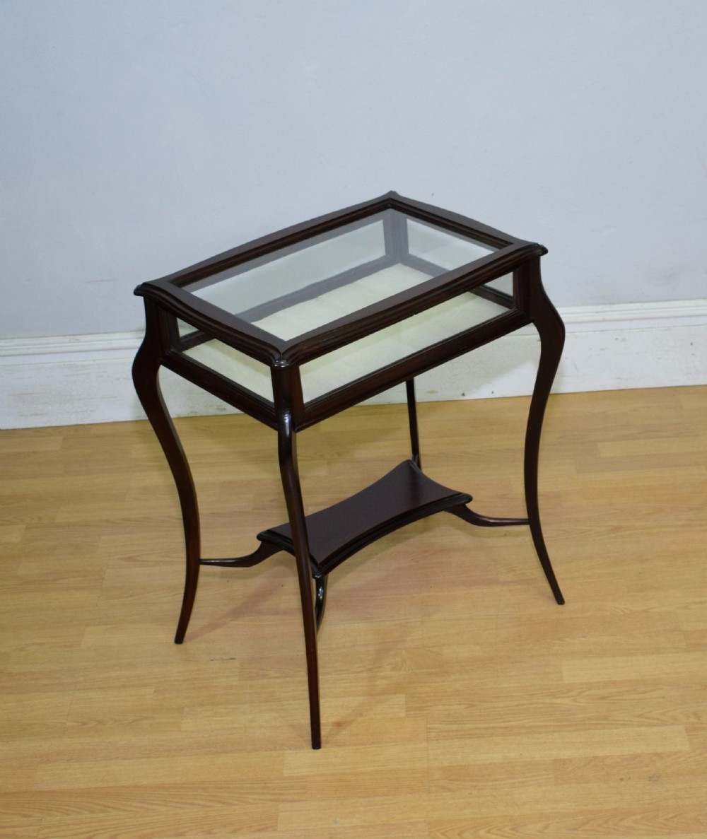 A Victorian dark mahogany bijouterie display table featuring four cabriole legs, clear glass side panels, a hinged glazed top, and a lower curved shelf.