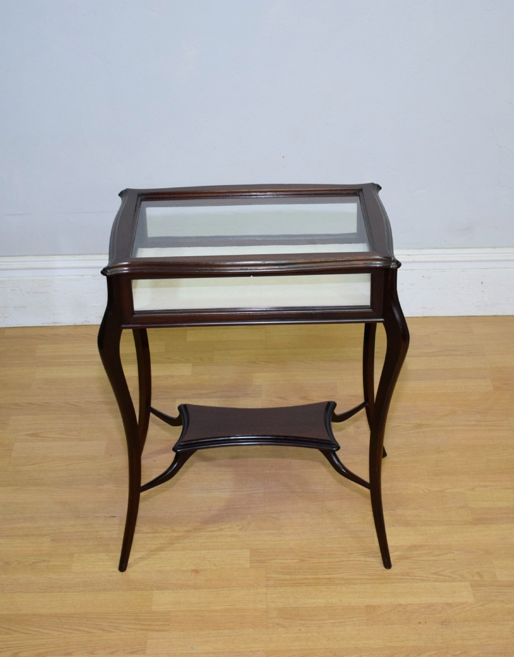 A Victorian dark mahogany bijouterie display table featuring four cabriole legs, clear glass side panels, a hinged glazed top, and a lower curved shelf. View VI