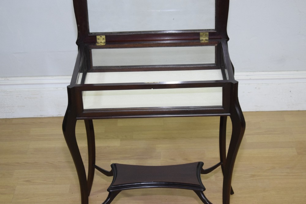 A Victorian dark mahogany bijouterie display table featuring four cabriole legs, clear glass side panels, a hinged glazed top, and a lower curved shelf. View X