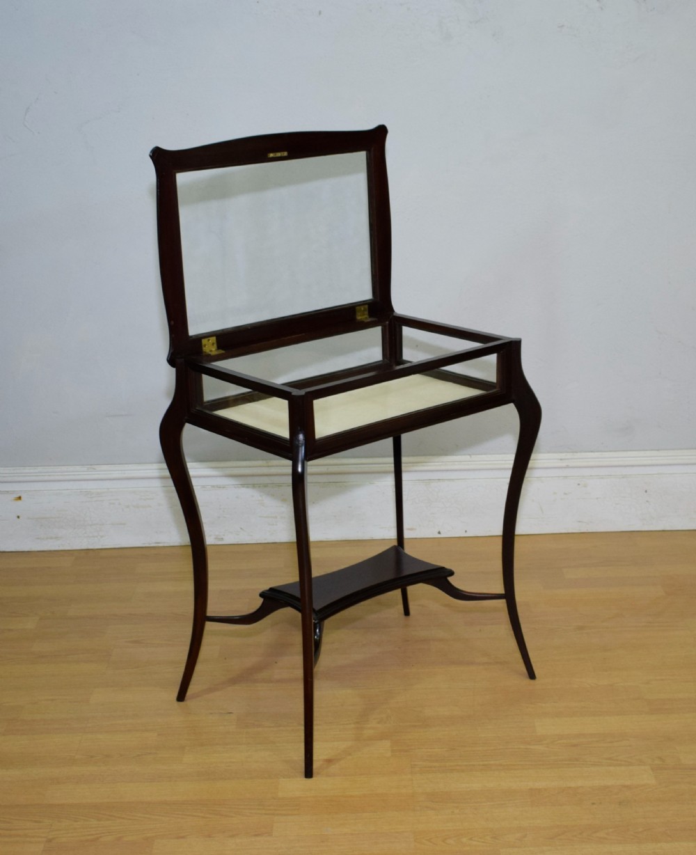 A Victorian dark mahogany bijouterie display table featuring four cabriole legs, clear glass side panels, a hinged glazed top, and a lower curved shelf. View XVI