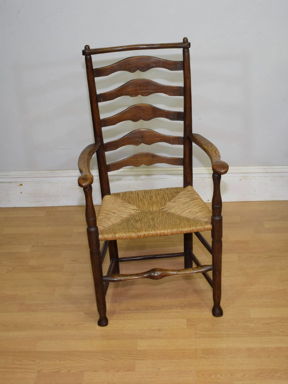 A 19th-century dark oak ladder-back armchair featuring five shaped horizontal back slats, turned legs, curved armrests, and a woven rush seat. View II