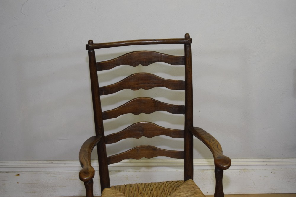 A 19th-century dark oak ladder-back armchair featuring five shaped horizontal back slats, turned legs, curved armrests, and a woven rush seat. View IV
