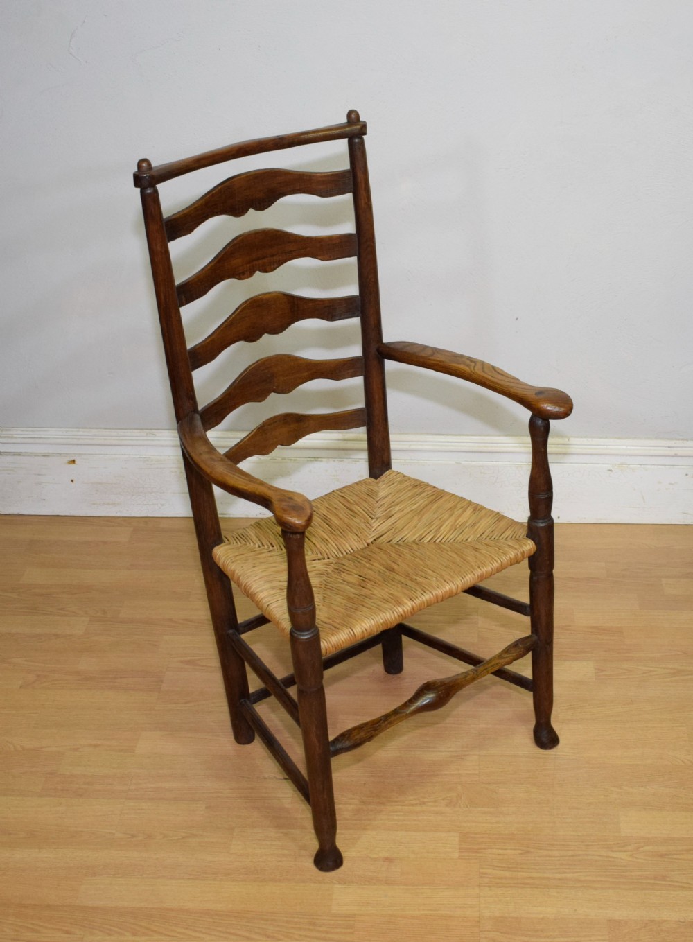 A 19th-century dark oak ladder-back armchair featuring five shaped horizontal back slats, turned legs, curved armrests, and a woven rush seat. View VIII
