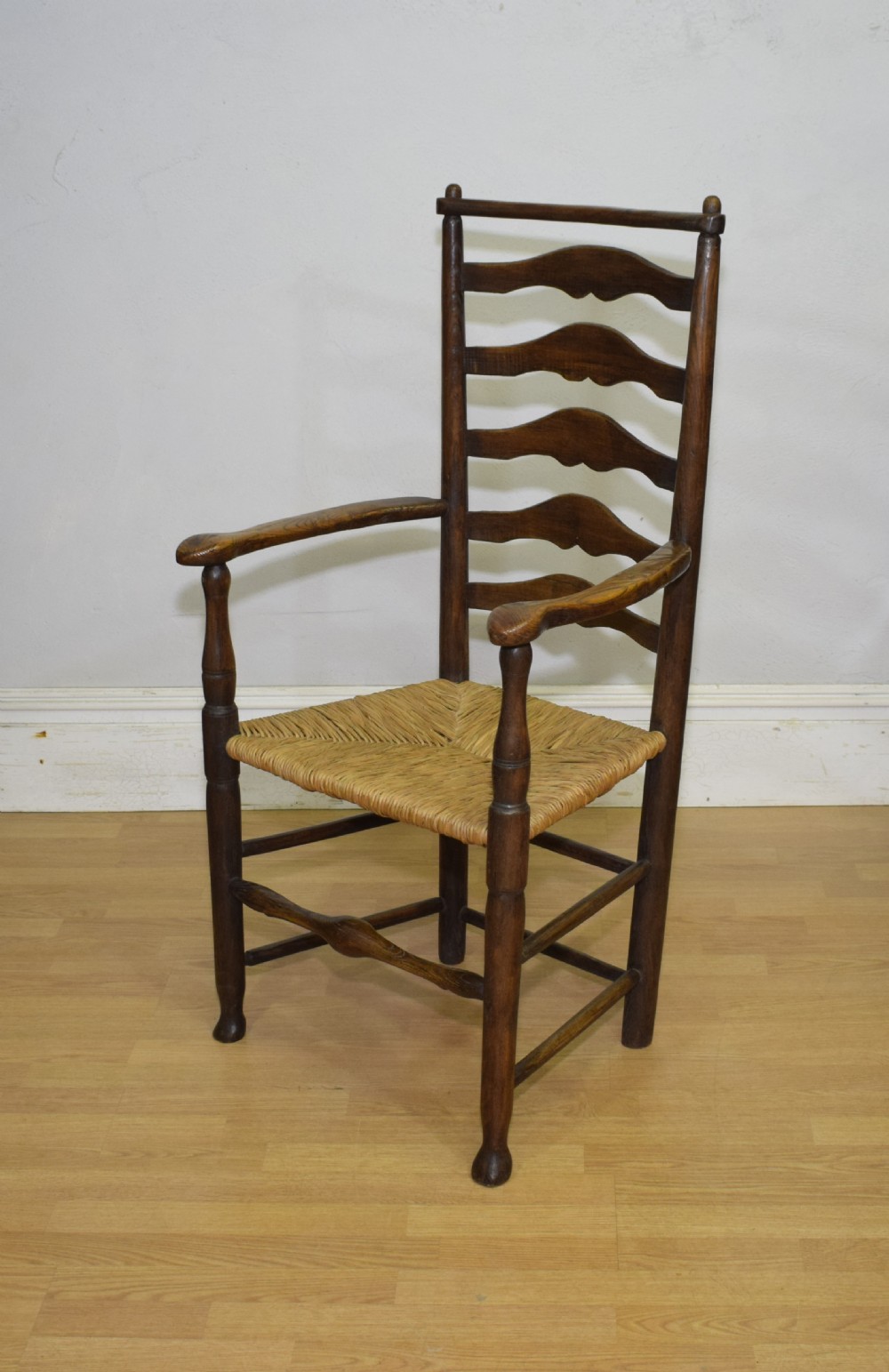 A 19th-century dark oak ladder-back armchair featuring five shaped horizontal back slats, turned legs, curved armrests, and a woven rush seat. View IX