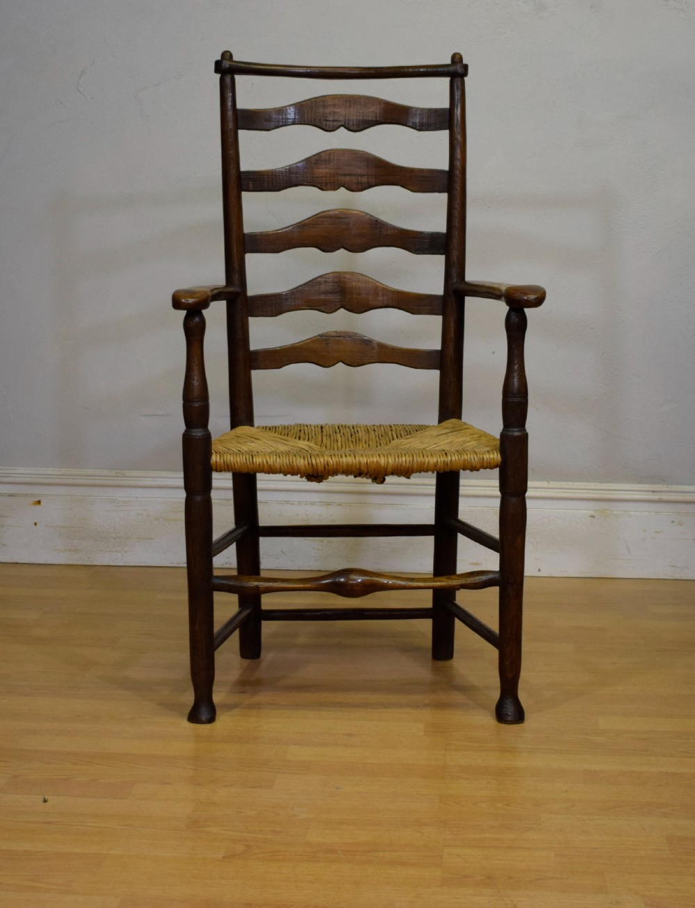 A 19th-century dark oak ladder-back armchair featuring five shaped horizontal back slats, turned legs, curved armrests, and a woven rush seat. View XI