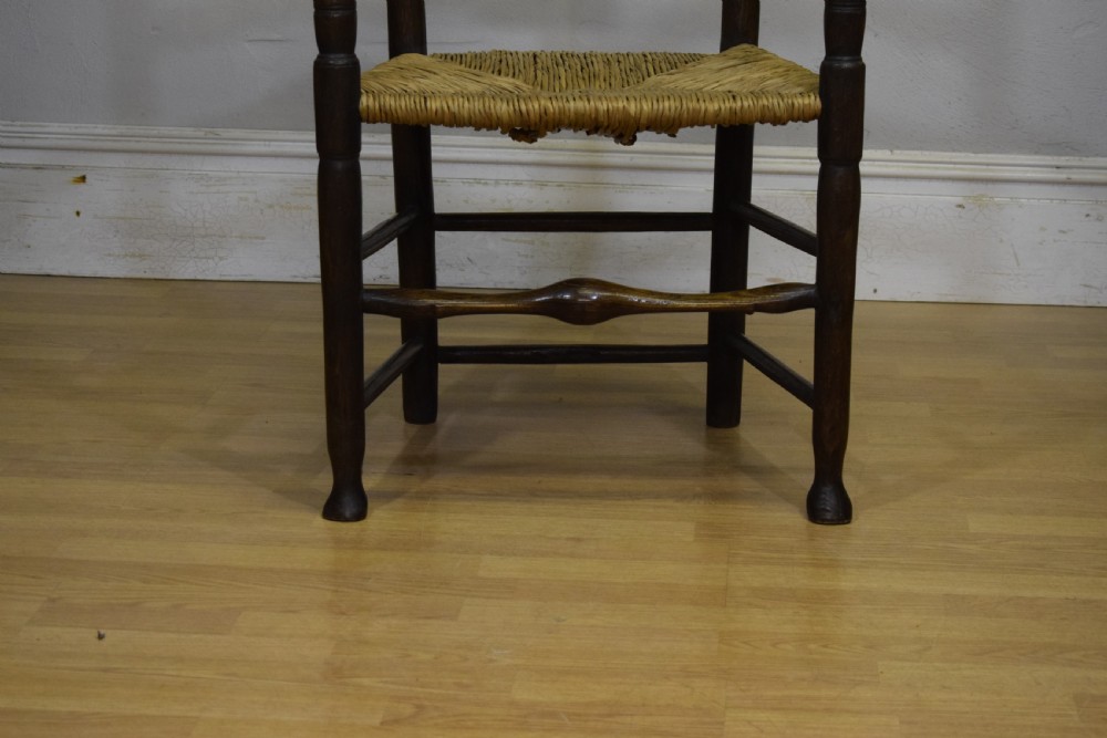 A 19th-century dark oak ladder-back armchair featuring five shaped horizontal back slats, turned legs, curved armrests, and a woven rush seat. View XII