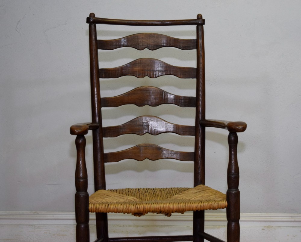 A 19th-century dark oak ladder-back armchair featuring five shaped horizontal back slats, turned legs, curved armrests, and a woven rush seat. View XIII