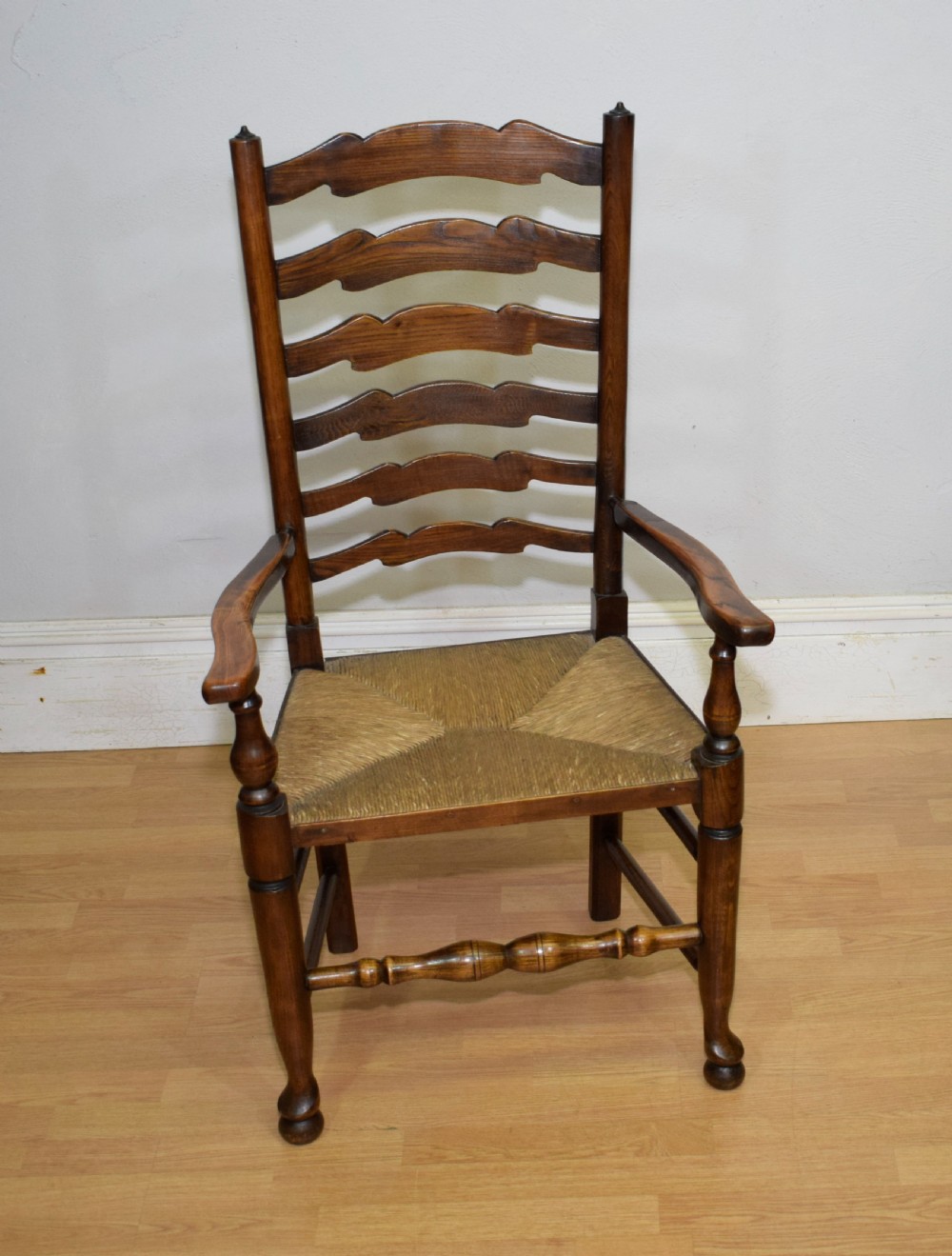 An early 20th-century oak ladderback armchair with curved arms, a hand-woven rush seat, and turned front legs joined by a decorative stretcher. View II