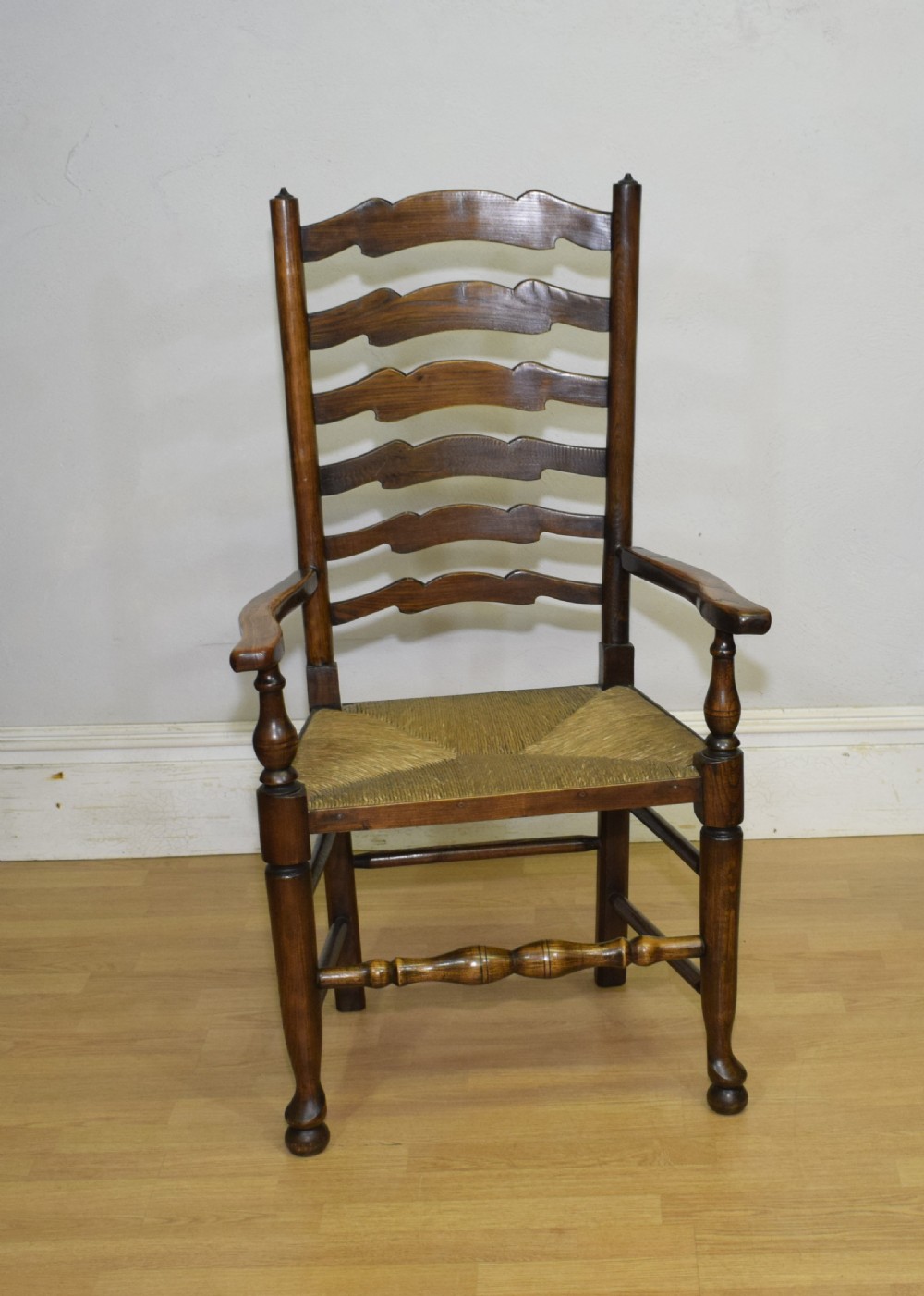 An early 20th-century oak ladderback armchair with curved arms, a hand-woven rush seat, and turned front legs joined by a decorative stretcher. View IV