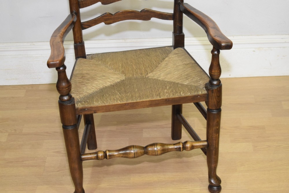 An early 20th-century oak ladderback armchair with curved arms, a hand-woven rush seat, and turned front legs joined by a decorative stretcher. View V