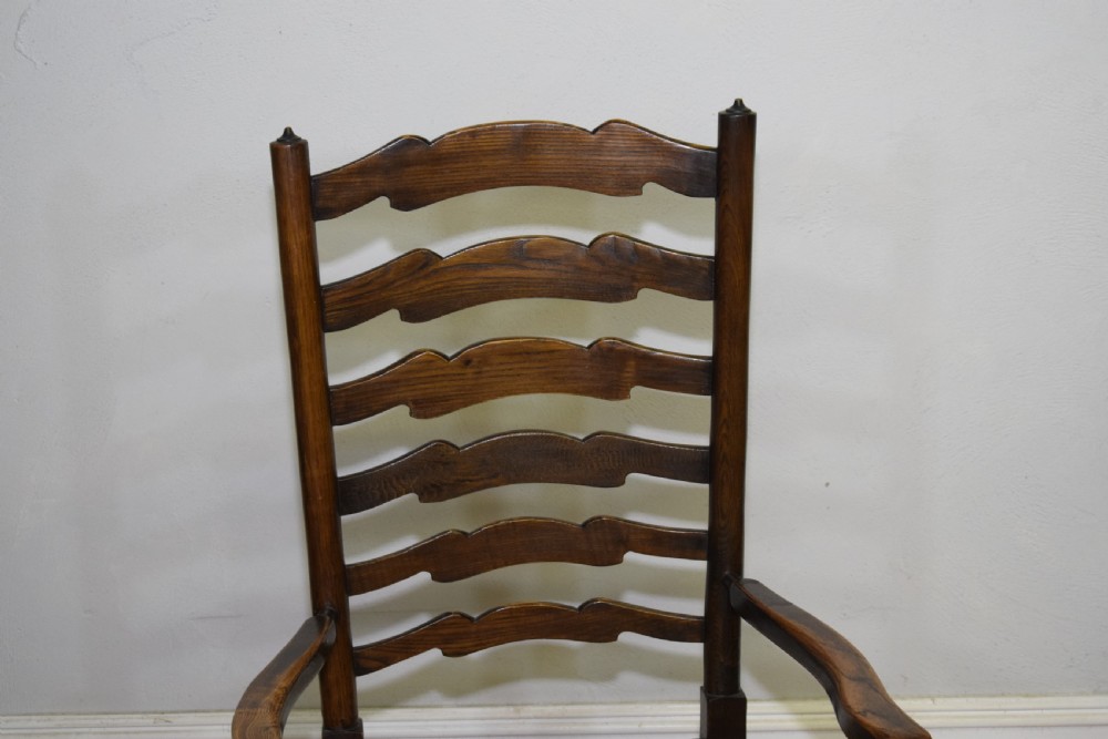 An early 20th-century oak ladderback armchair with curved arms, a hand-woven rush seat, and turned front legs joined by a decorative stretcher. View VI