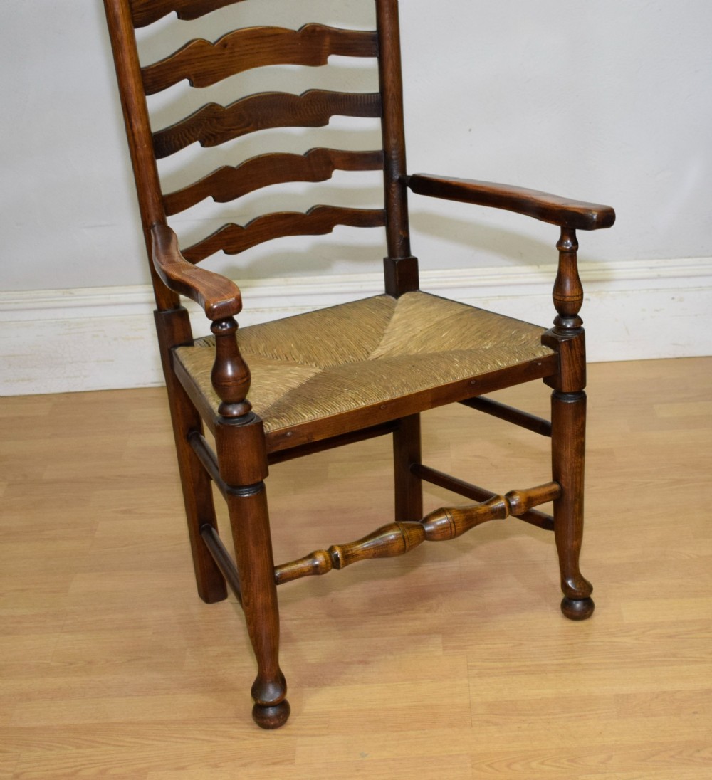 An early 20th-century oak ladderback armchair with curved arms, a hand-woven rush seat, and turned front legs joined by a decorative stretcher. View X