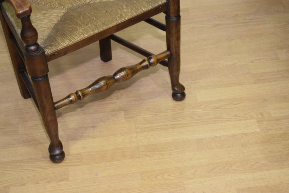 An early 20th-century oak ladderback armchair with curved arms, a hand-woven rush seat, and turned front legs joined by a decorative stretcher. View XII