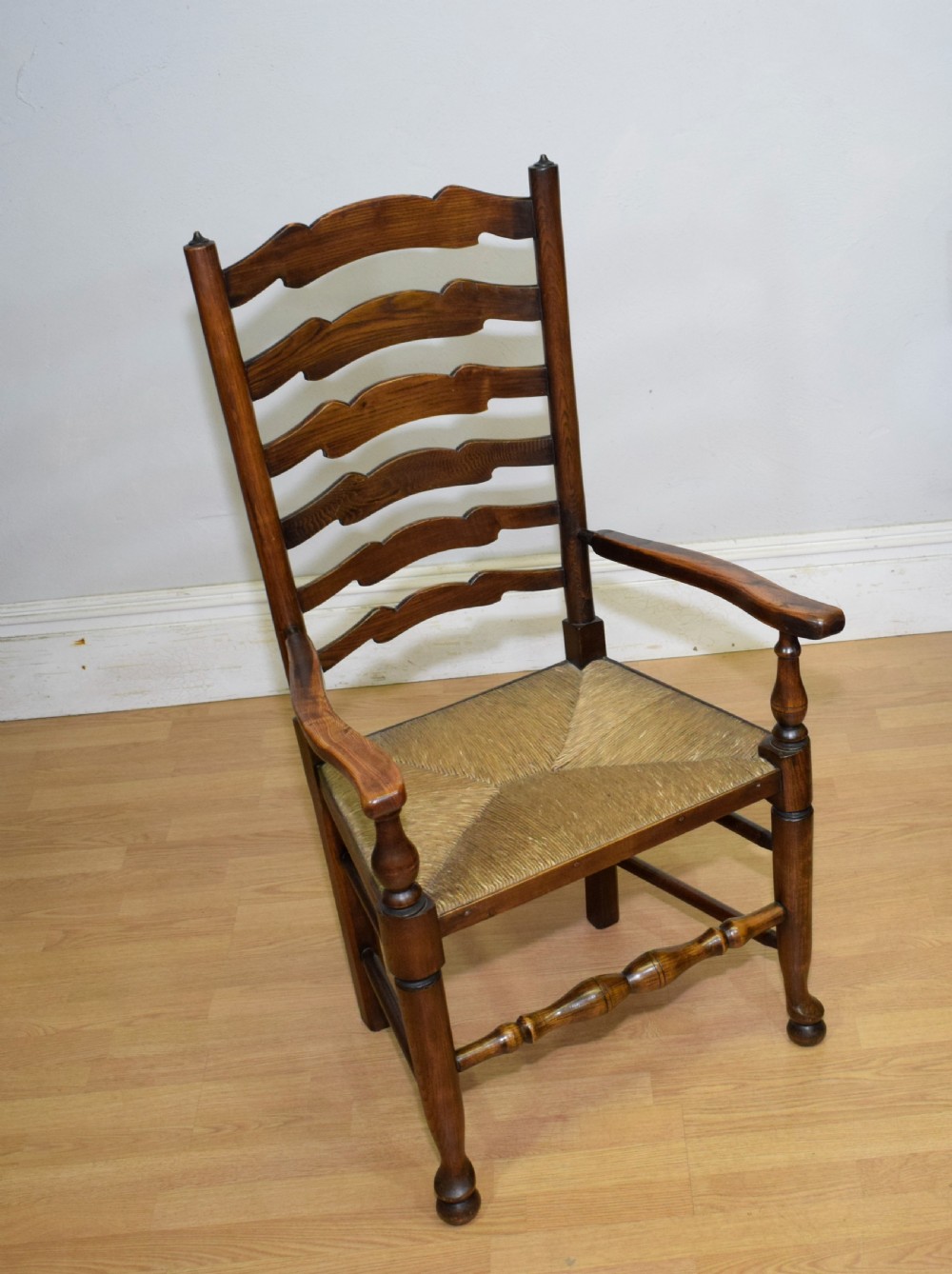 An early 20th-century oak ladderback armchair with curved arms, a hand-woven rush seat, and turned front legs joined by a decorative stretcher. View XIII