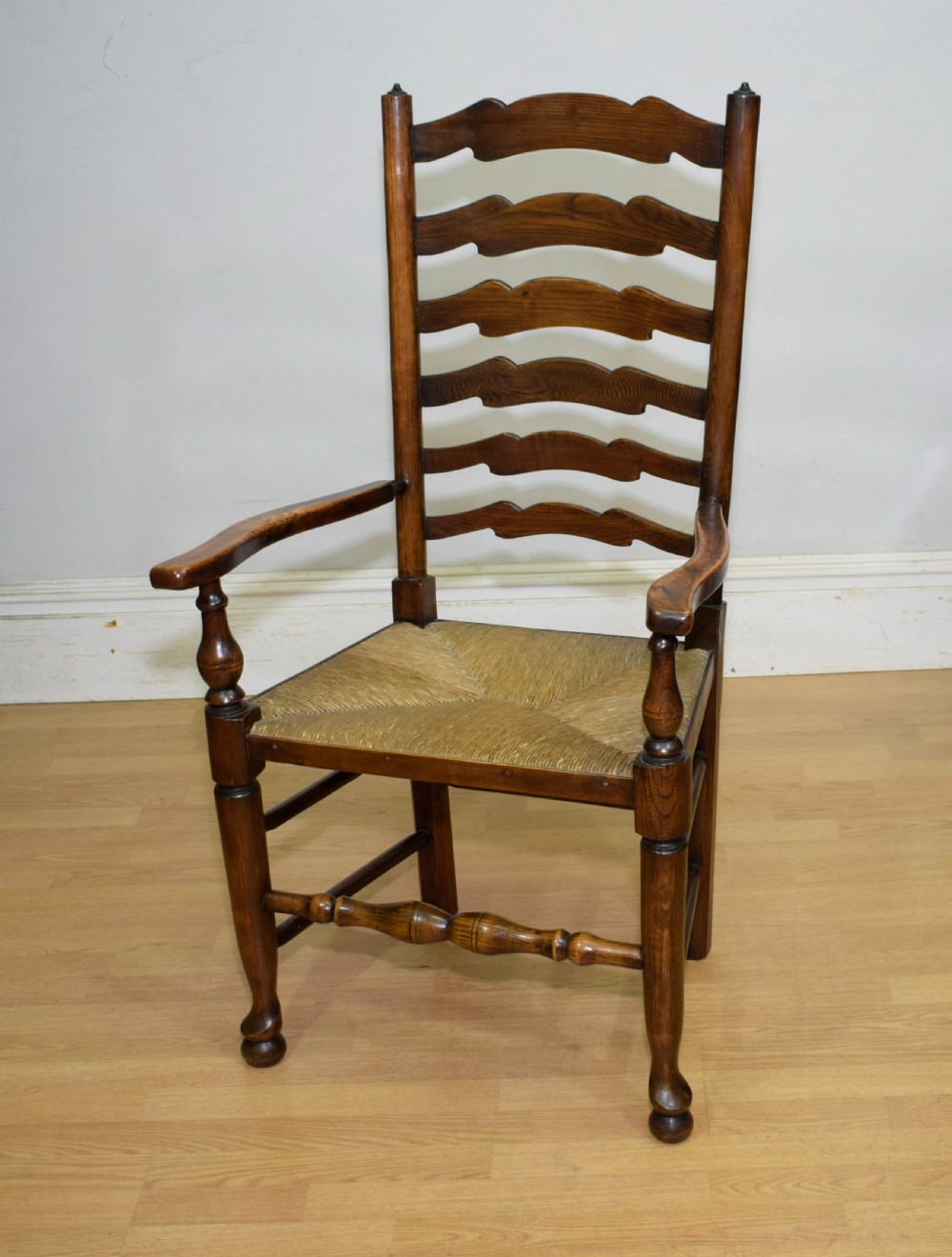 An early 20th-century oak ladderback armchair with curved arms, a hand-woven rush seat, and turned front legs joined by a decorative stretcher. View XVI
