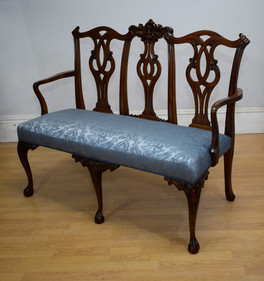 An early 20th-century mahogany triple chair-back Chippendale style settee featuring carved pierced back splats, light blue patterned upholstery, and cabriole legs with ball-and-claw feet.