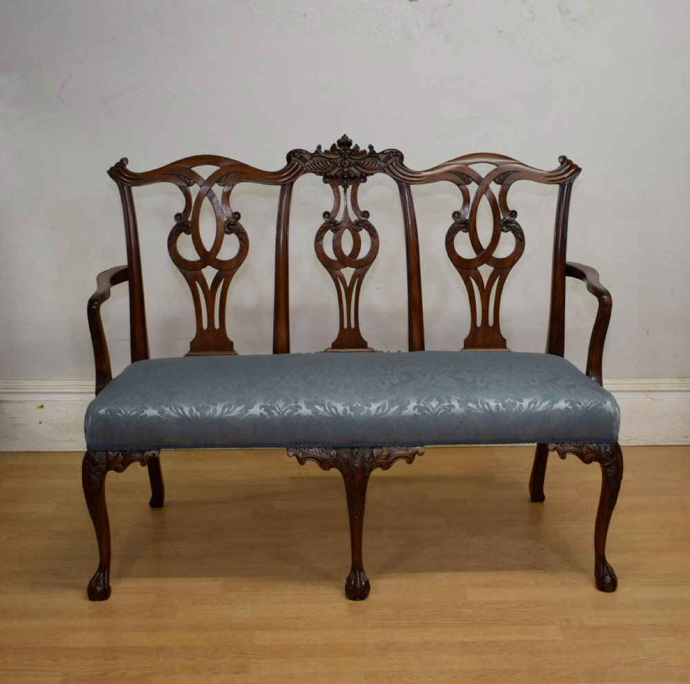 An early 20th-century mahogany triple chair-back Chippendale style settee featuring carved pierced back splats, light blue patterned upholstery, and cabriole legs with ball-and-claw feet. View II