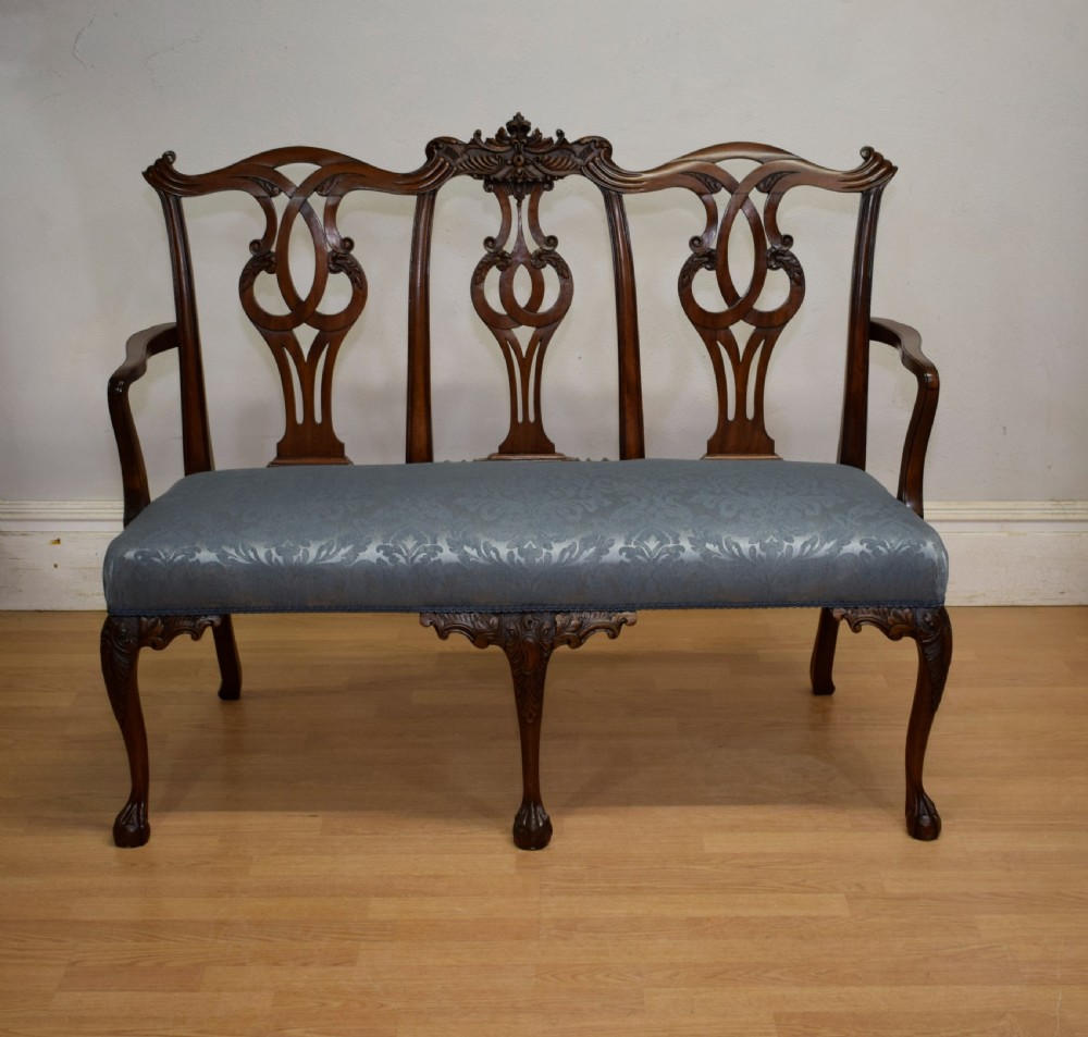 An early 20th-century mahogany triple chair-back Chippendale style settee featuring carved pierced back splats, light blue patterned upholstery, and cabriole legs with ball-and-claw feet. View V