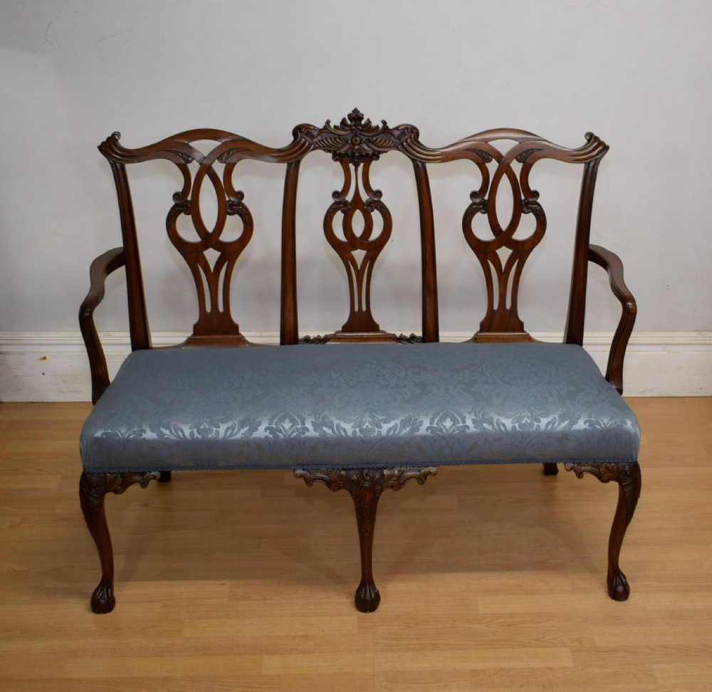 An early 20th-century mahogany triple chair-back Chippendale style settee featuring carved pierced back splats, light blue patterned upholstery, and cabriole legs with ball-and-claw feet. View VI