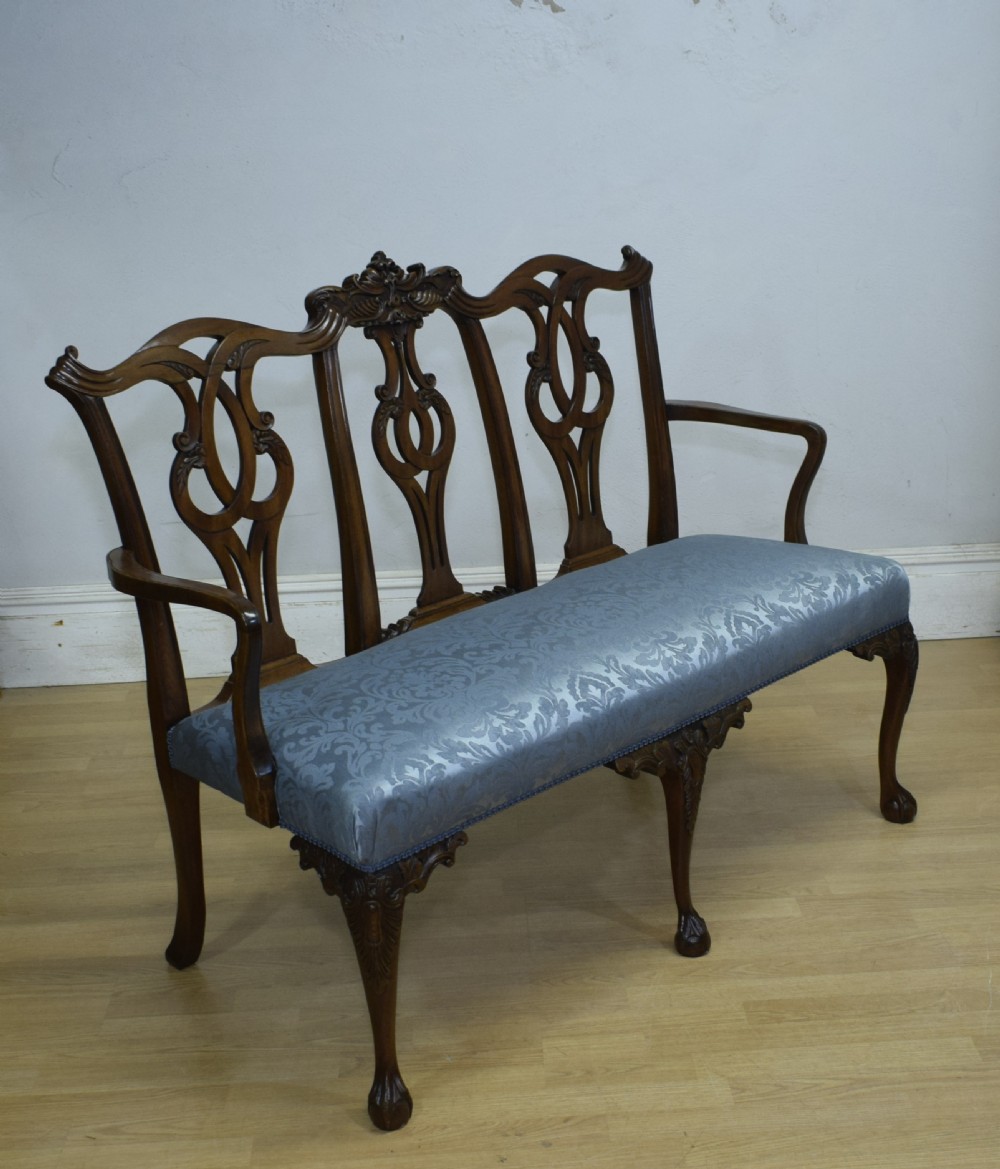 An early 20th-century mahogany triple chair-back Chippendale style settee featuring carved pierced back splats, light blue patterned upholstery, and cabriole legs with ball-and-claw feet. View XII