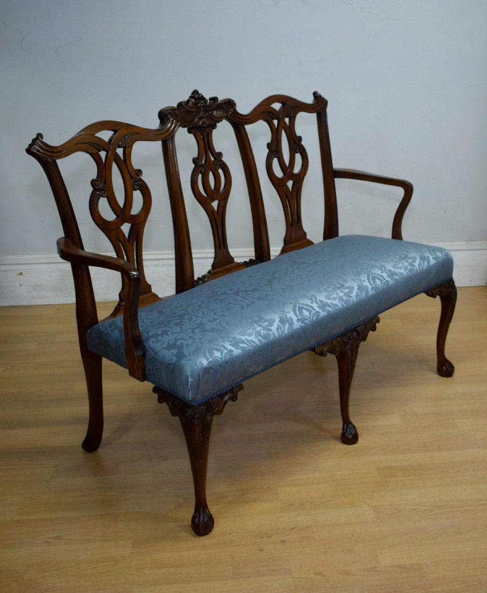 An early 20th-century mahogany triple chair-back Chippendale style settee featuring carved pierced back splats, light blue patterned upholstery, and cabriole legs with ball-and-claw feet. View XIV