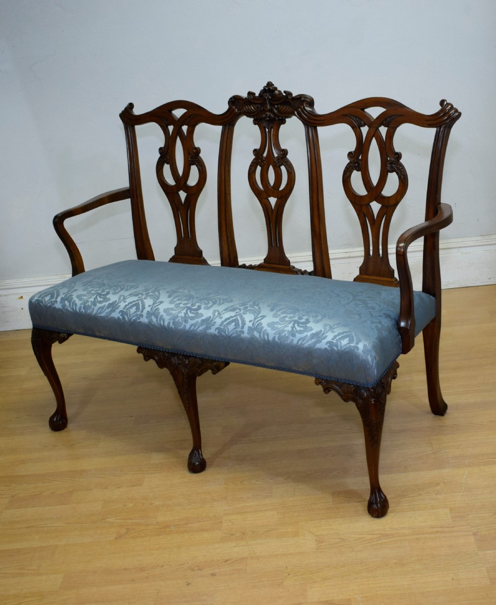 An early 20th-century mahogany triple chair-back Chippendale style settee featuring carved pierced back splats, light blue patterned upholstery, and cabriole legs with ball-and-claw feet. View XV