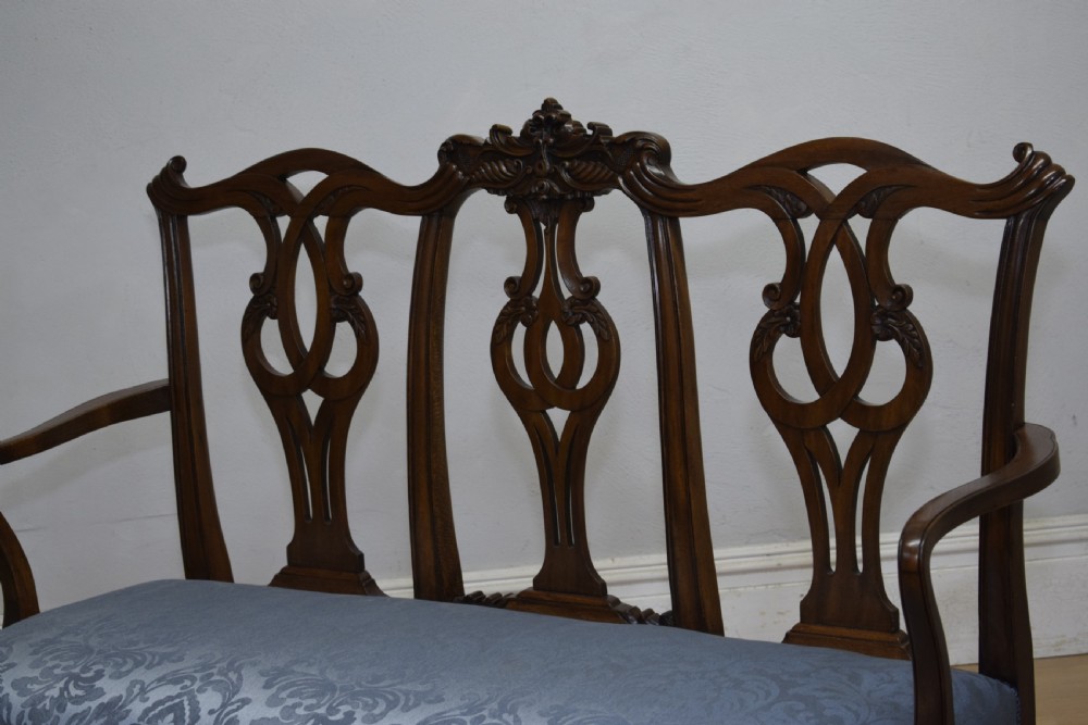 An early 20th-century mahogany triple chair-back Chippendale style settee featuring carved pierced back splats, light blue patterned upholstery, and cabriole legs with ball-and-claw feet. View XVI