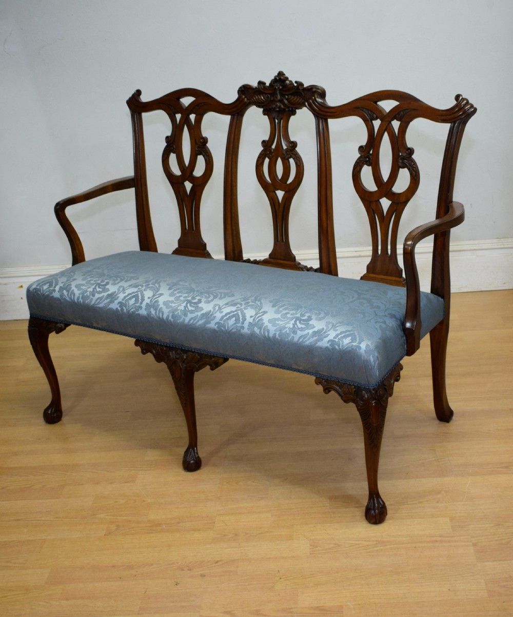 An early 20th-century mahogany triple chair-back Chippendale style settee featuring carved pierced back splats, light blue patterned upholstery, and cabriole legs with ball-and-claw feet. View XVII