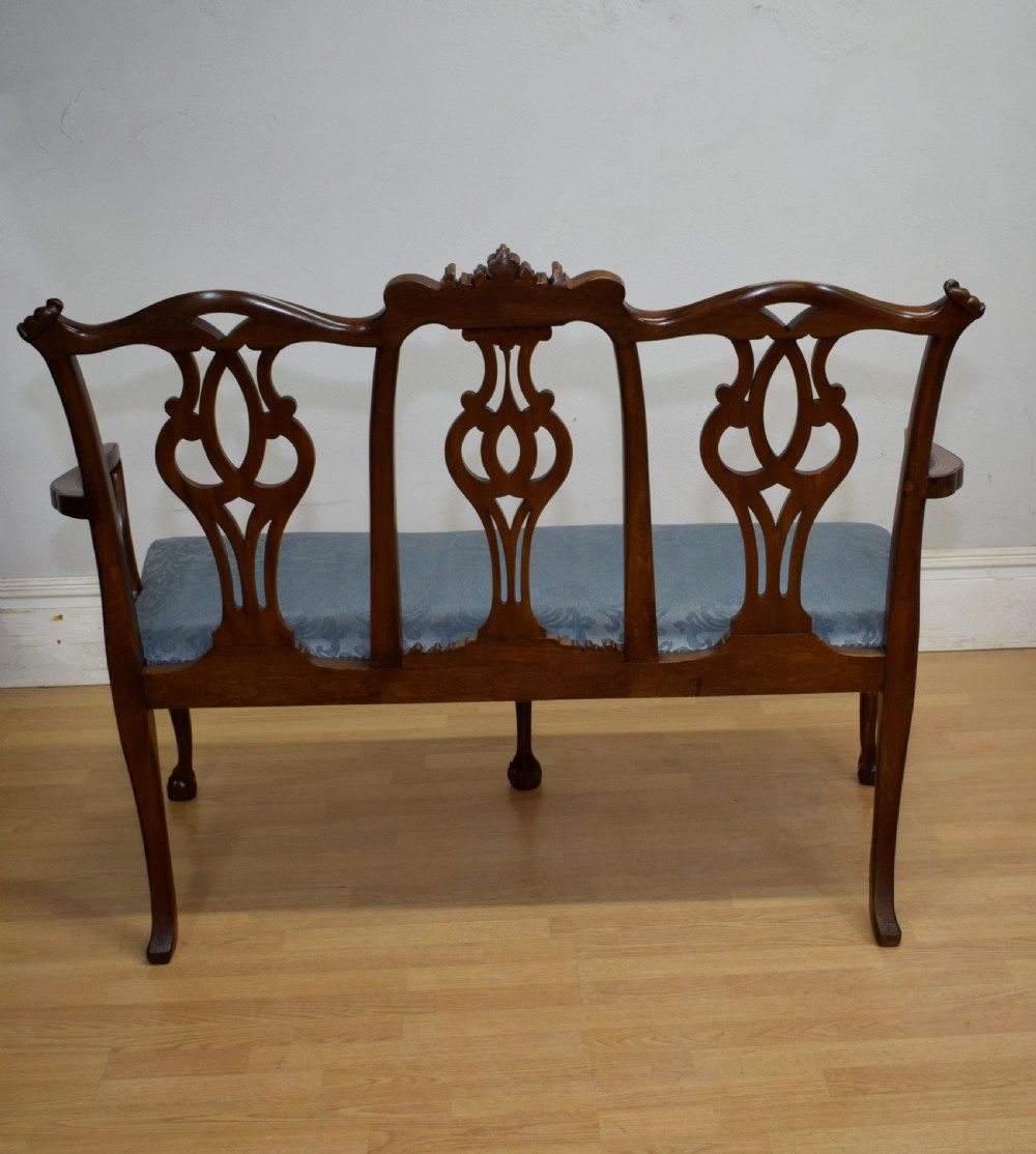 An early 20th-century mahogany triple chair-back Chippendale style settee featuring carved pierced back splats, light blue patterned upholstery, and cabriole legs with ball-and-claw feet. View XX