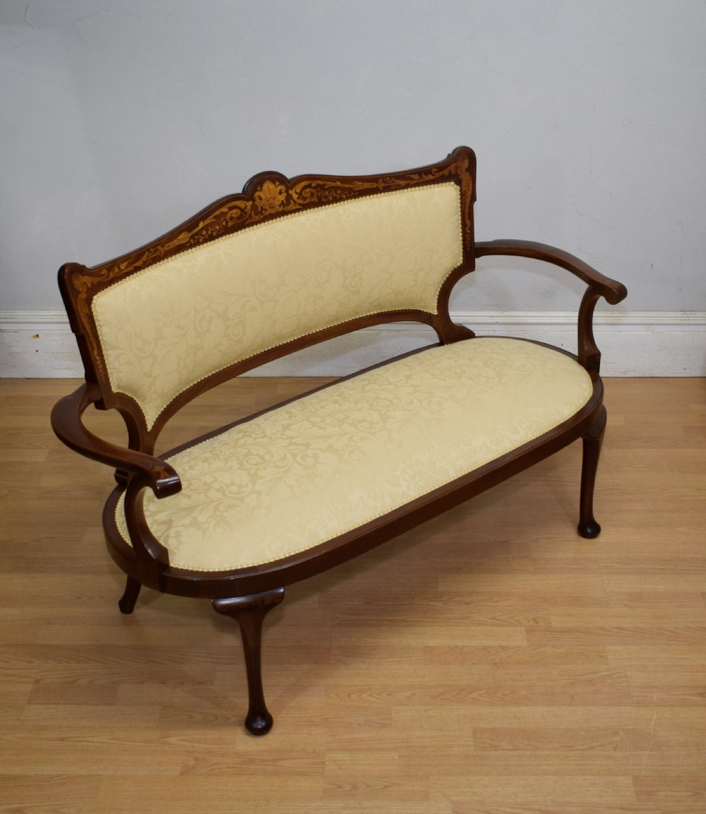 A Victorian dark mahogany settee with floral marquetry inlay along the crest rail and cream damask upholstered seat and backrest.