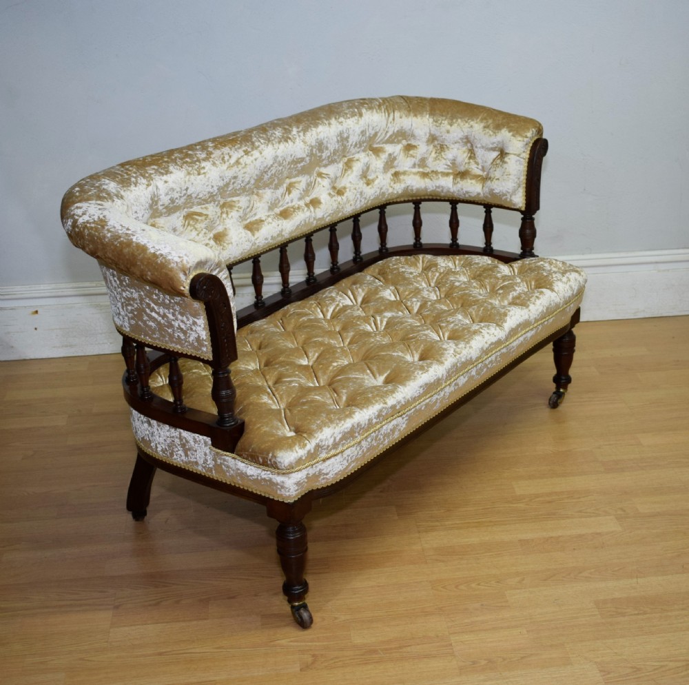 A Victorian mahogany settee with champagne gold crushed velvet deep-buttoned upholstery, a spindle gallery back, and turned legs with castors.